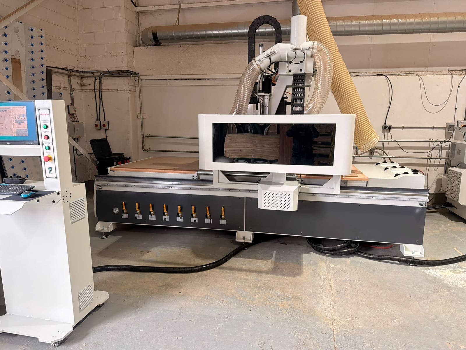 A Hua Hua CNC router with its control console in a small workshop unit, extraction hose running up to the ceiling